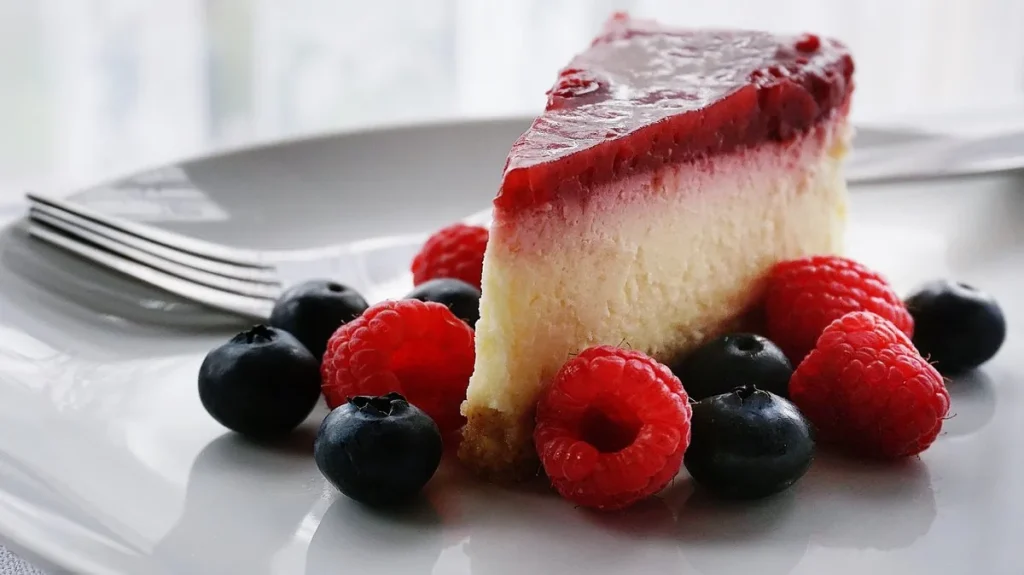 Stück Beerentorte mit Himbeeren und Heidelbeeren auf weißem Teller
