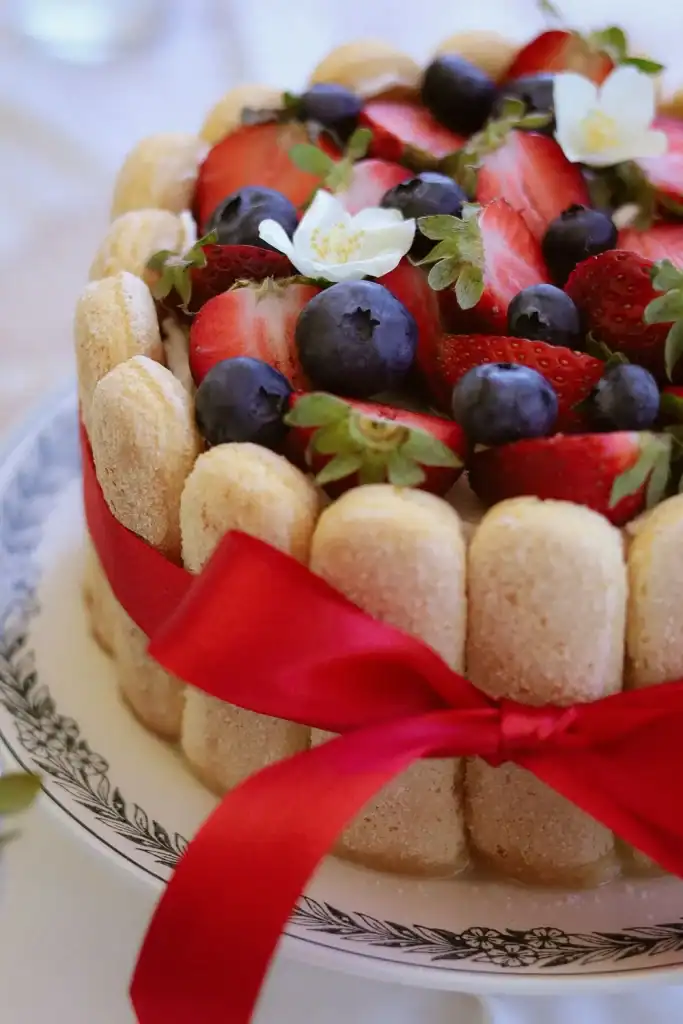 Frische Obsttorte mit Beeren, Biskuit und roter Schleife.