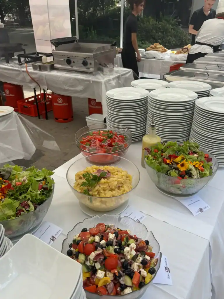 Buffet mit Salaten, Vorspeisen und Geschirr in einer Veranstaltungshalle.
