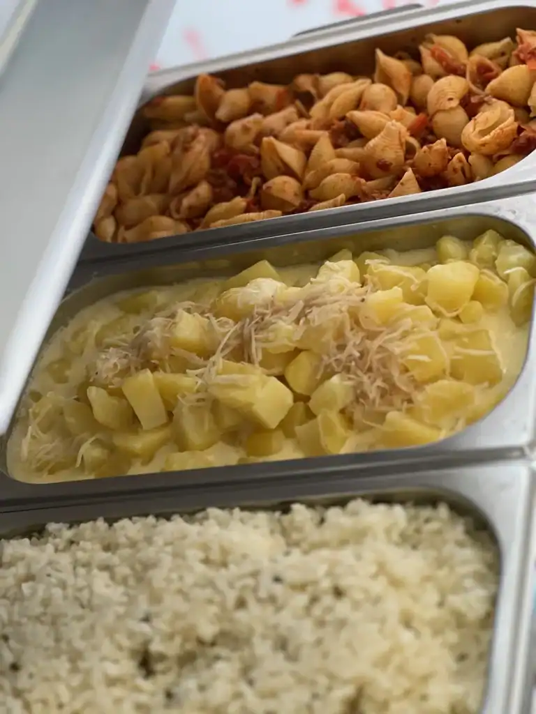 Verschiedene Speisen in Buffet-Behältern, Pasta, Kartoffeln und Reis.