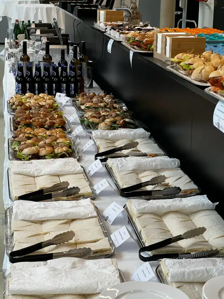 Buffet mit verschiedenen Snacks, Getränken und Besteck auf einer Veranstaltung.
